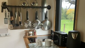 Eine Küche mit hängenden Töpfen und Pfannen, einer Kaffeemaschine, einem Toaster und einem Fenster mit Blick ins Grüne.