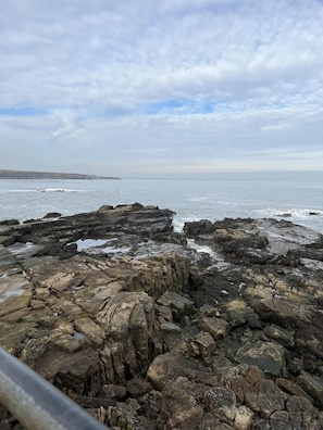 A rocky coastline with waves crashing against the rocks under a cloudy sky.