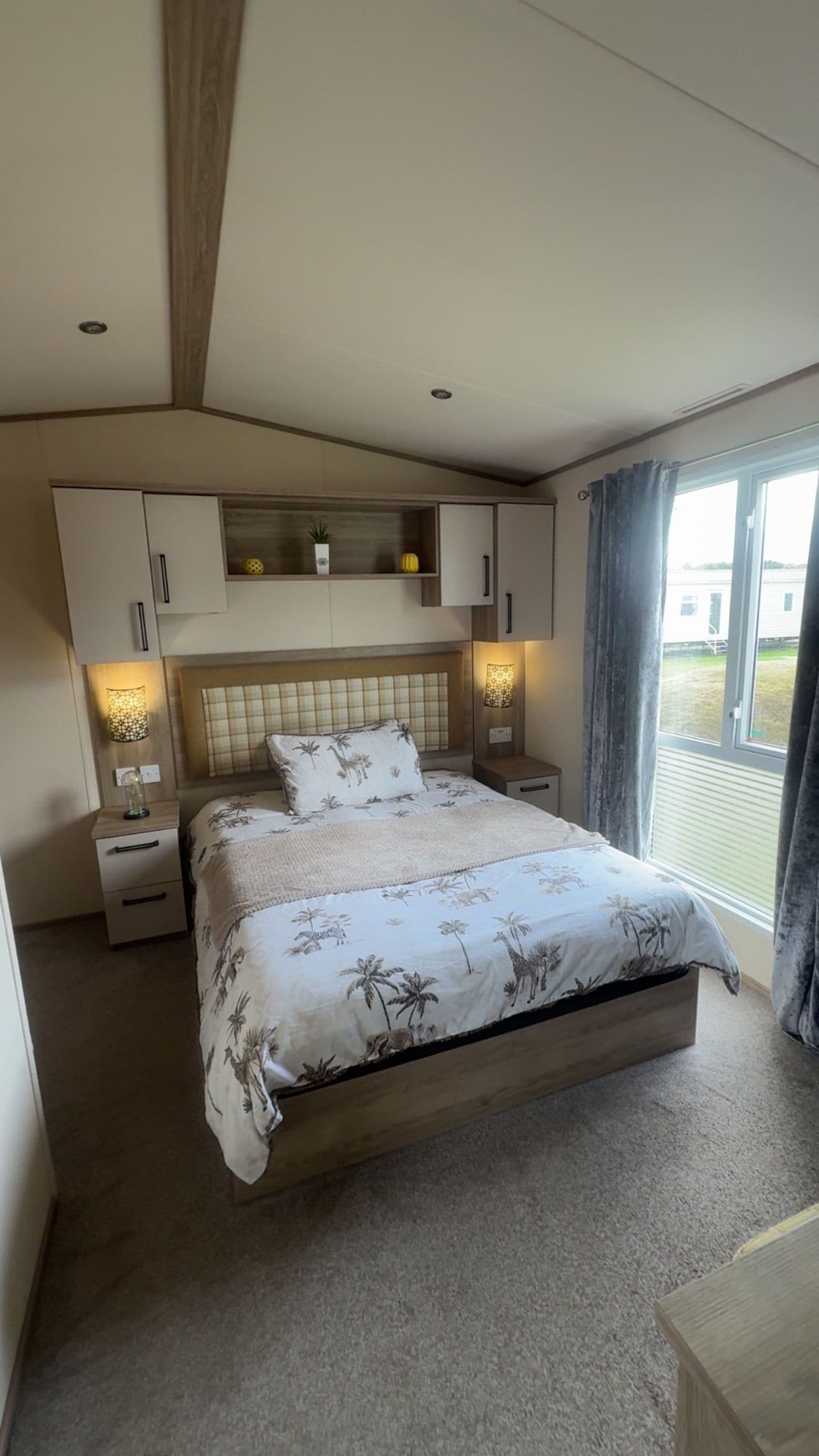 A bedroom with a large bed, bedside tables, a headboard, and a window with curtains.