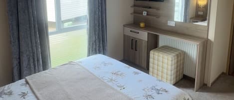 A bedroom with a bed, a desk, a television, and a window with curtains.
