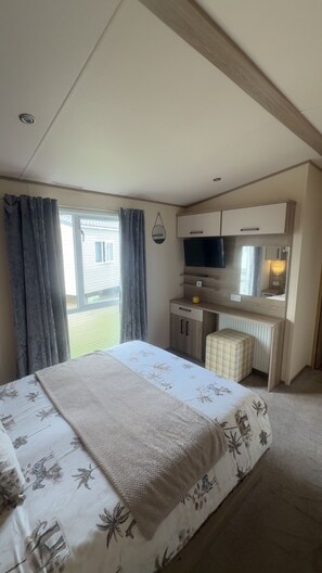 A bedroom with a bed, a desk, a television, and a window with curtains. - 2 Bed Caravan - Sleeps 5  Parking - Pets (Whitley Bay)