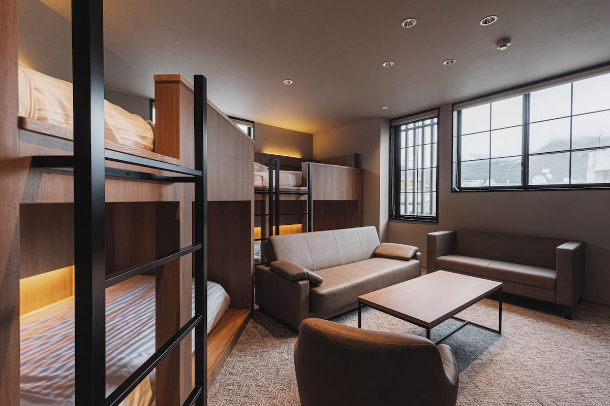 Una habitación de hotel moderna con literas, un sofá, una mesa de centro y ventanas amplias que dejan entrar luz natural.
