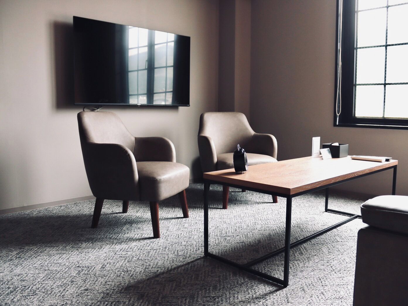 Una sala de conferencias con dos sillones de cuero, una mesa de madera, un altavoz negro y un televisor de pantalla plana montado en la pared.
