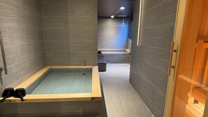 Un spa moderno con una bañera grande, un banco de madera y una zona de ducha con mampara de vidrio.