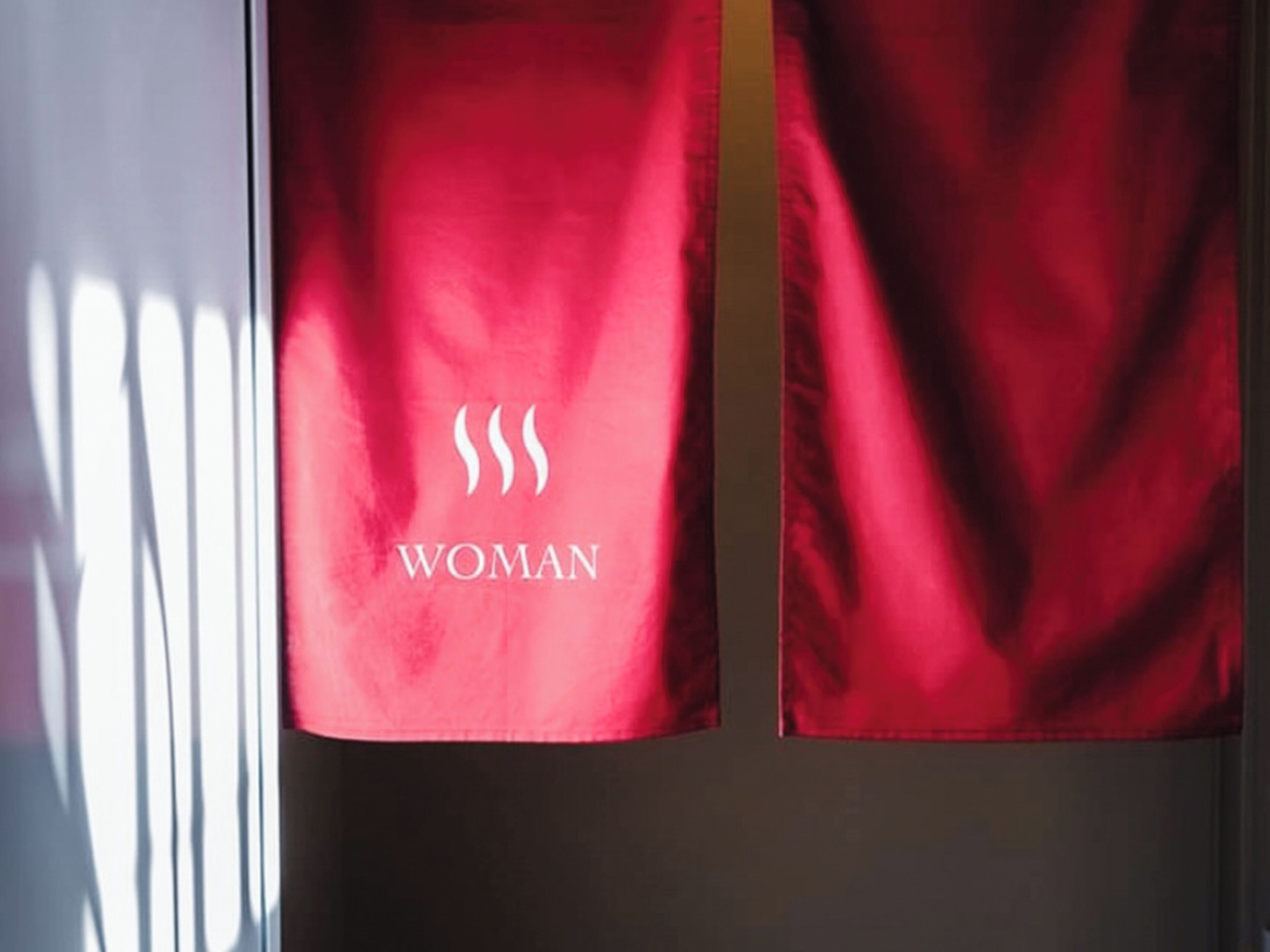 A red banner with the word "WOMAN" and a symbol of three wavy lines.