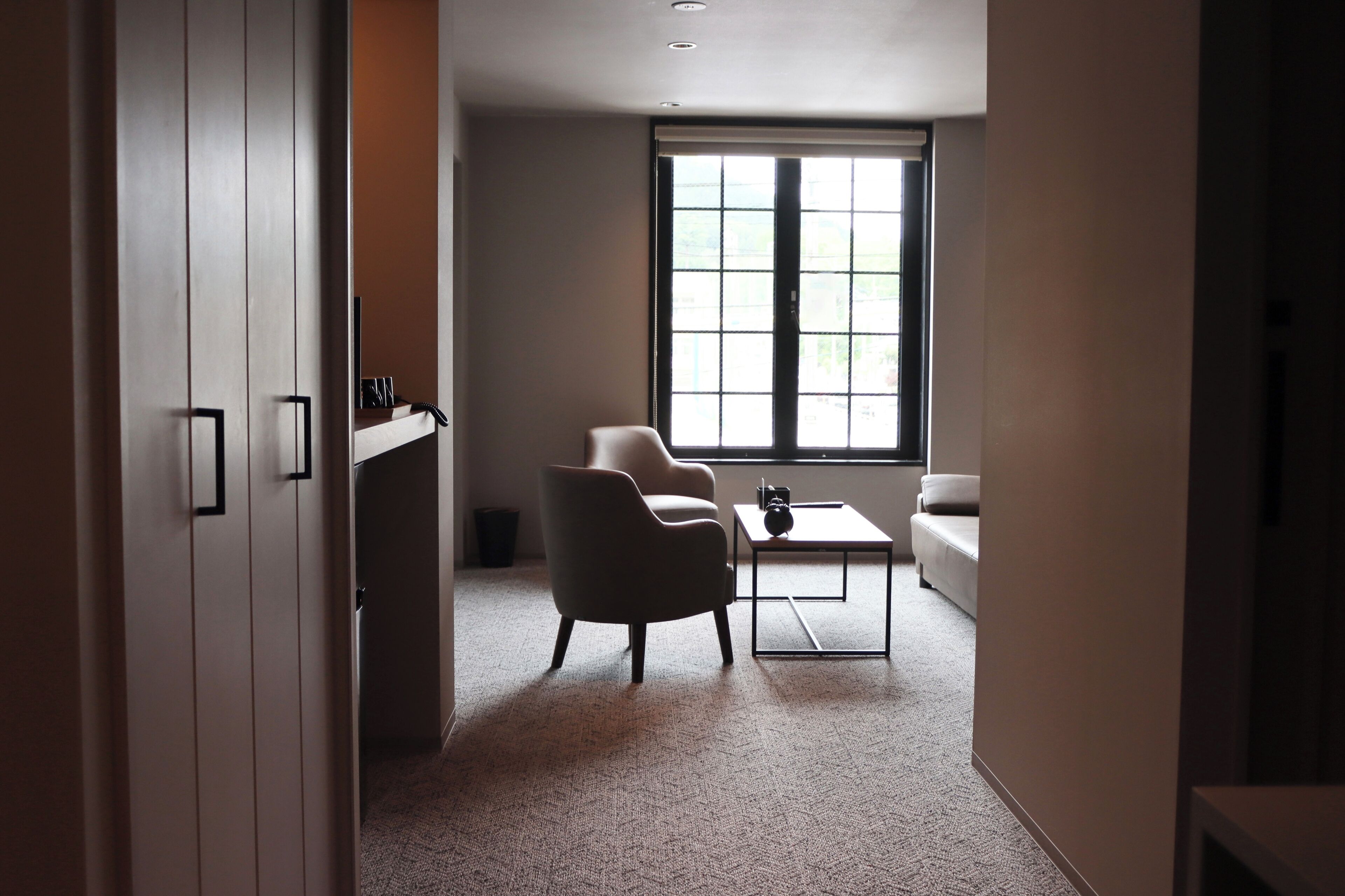 Una habitación moderna con un ventanal grande, un sofá, una silla y una mesita.