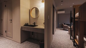 Una habitación de hotel moderna con un espejo redondo grande, un lavabo, una silla, un armario y una cama litera.