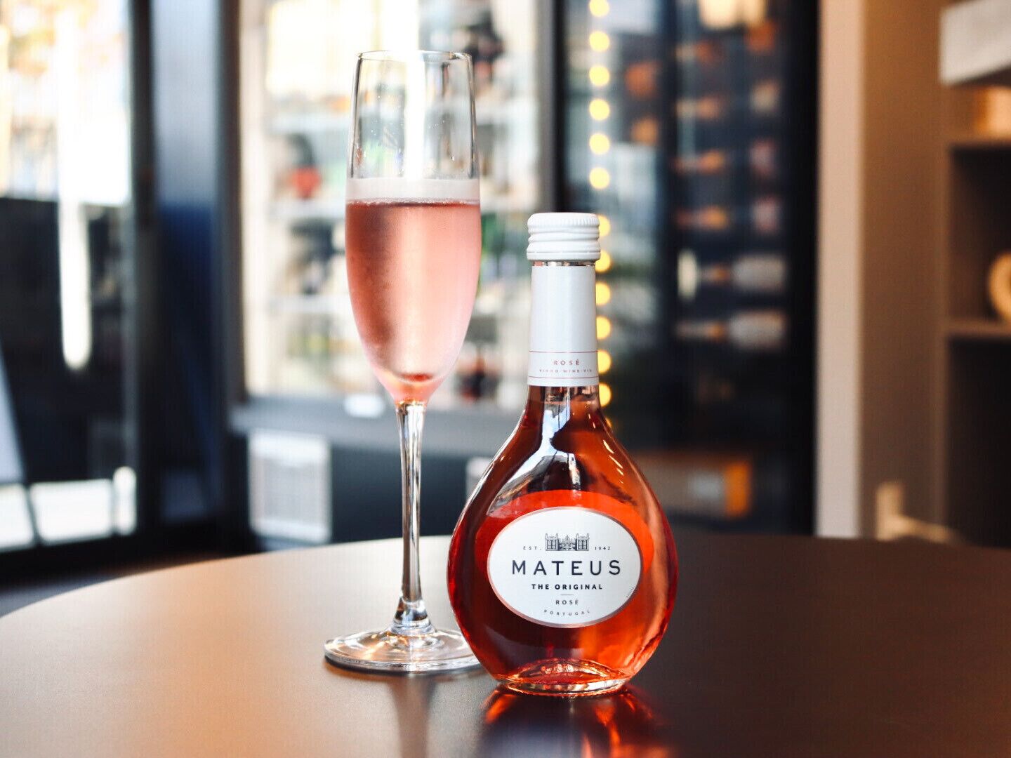 A bottle of Mateus wine and a glass of rosé wine on a table.