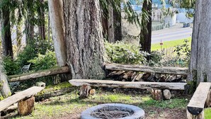 Un foyer circulaire en pierre, entouré d’une clôture en bois et de bancs.