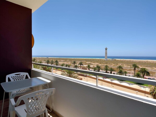 A balcony with a view of the beach, a lighthouse, and palm trees.