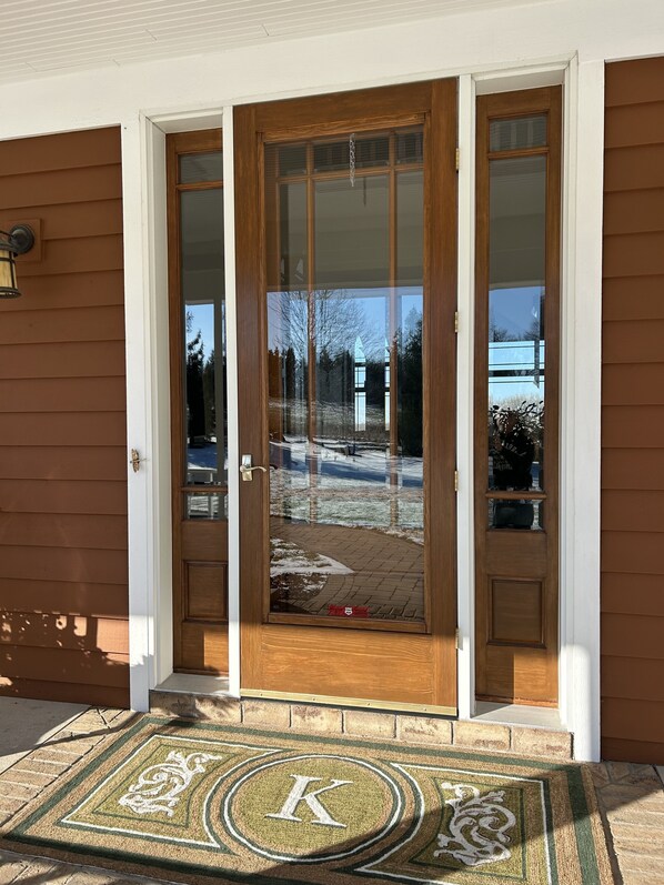 A wooden front door with a glass panel, a doormat with a letter 'K', and a brick pathway leading to the door. - Horse Ranch Gem (Pickett)