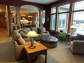 A spacious living room with a large window, a dining area, and a kitchen in the background. - Horse Ranch Gem (Pickett)