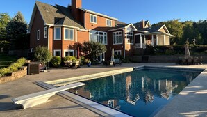 Een groot huis met een zwembad, een overdekt terras en een aangelegde tuin.