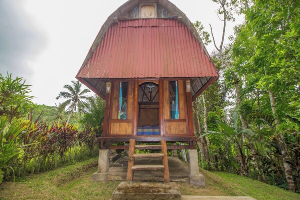 A wooden structure with a red roof, surrounded by lush greenery.