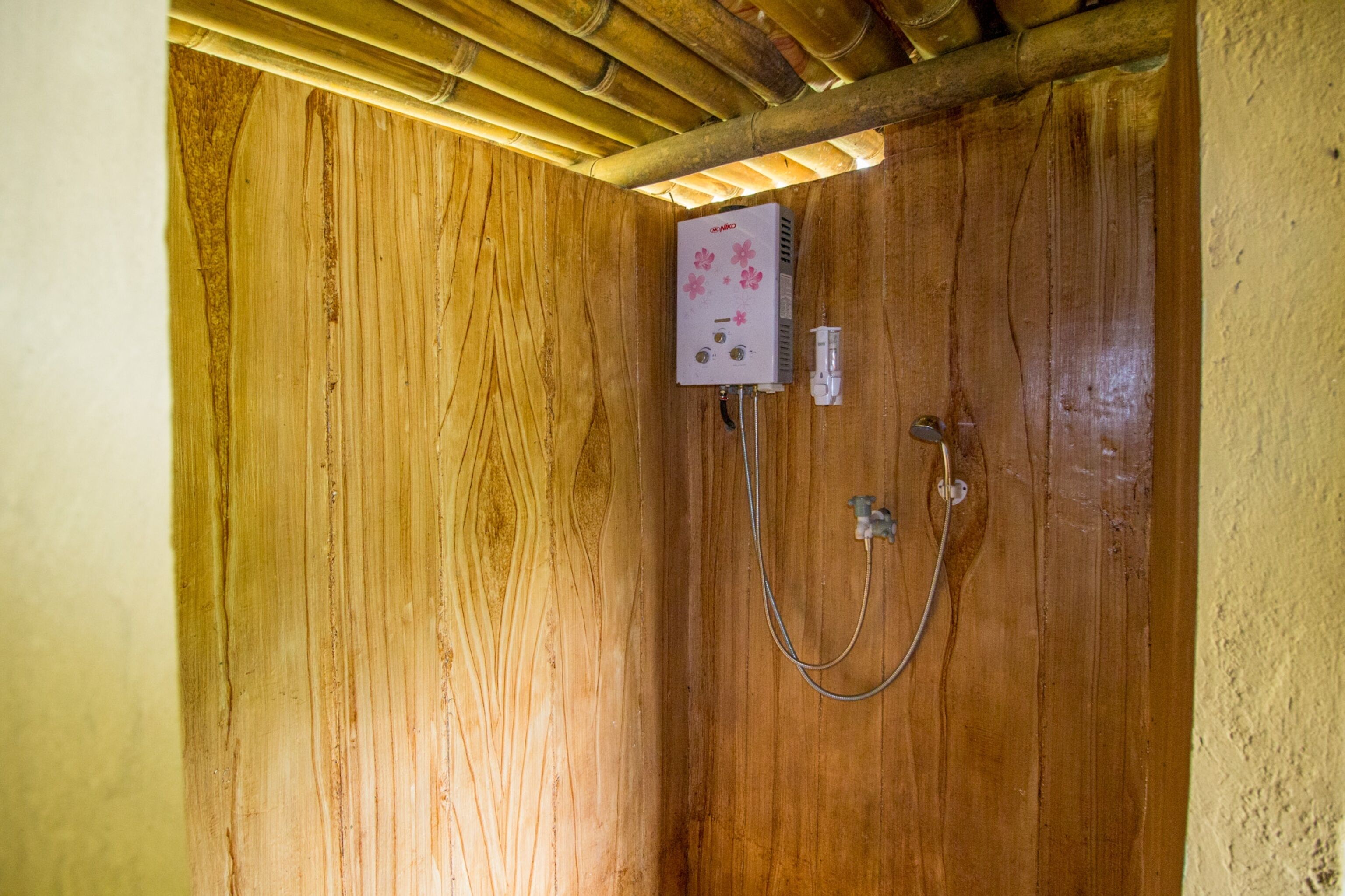 Um banheiro de madeira com chuveiro embutido, um aquecedor branco com flores cor-de-rosa e uma pequena tomada elétrica.