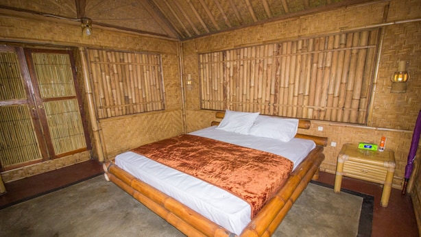 A room with a large bed, bamboo walls, and a small wooden nightstand with a lamp. - Pesona Bali Ecolodge (Penebel)