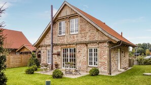 Een stenen huis met twee verdiepingen, voorzien van een rode dakbedekking, een schoorsteen en een klein terras met tuinmeubilair.