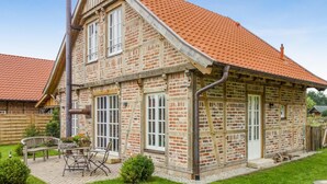 Een tweelaags huis met een rode dakbedekking, een bakstenen gevel en een terras met tuinmeubilair.