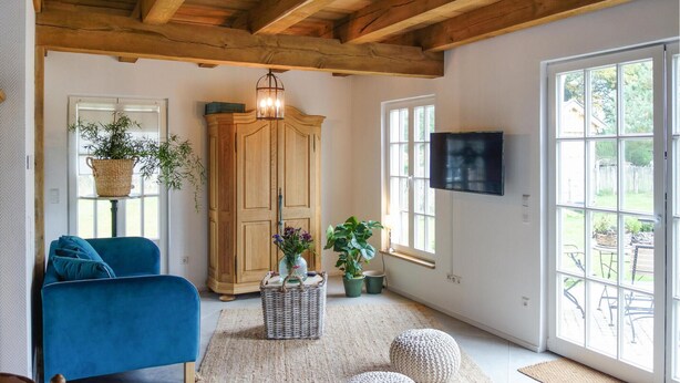 Een woonkamer met een blauwe bank, een houten kast, een rieten mand en een televisie aan de muur.