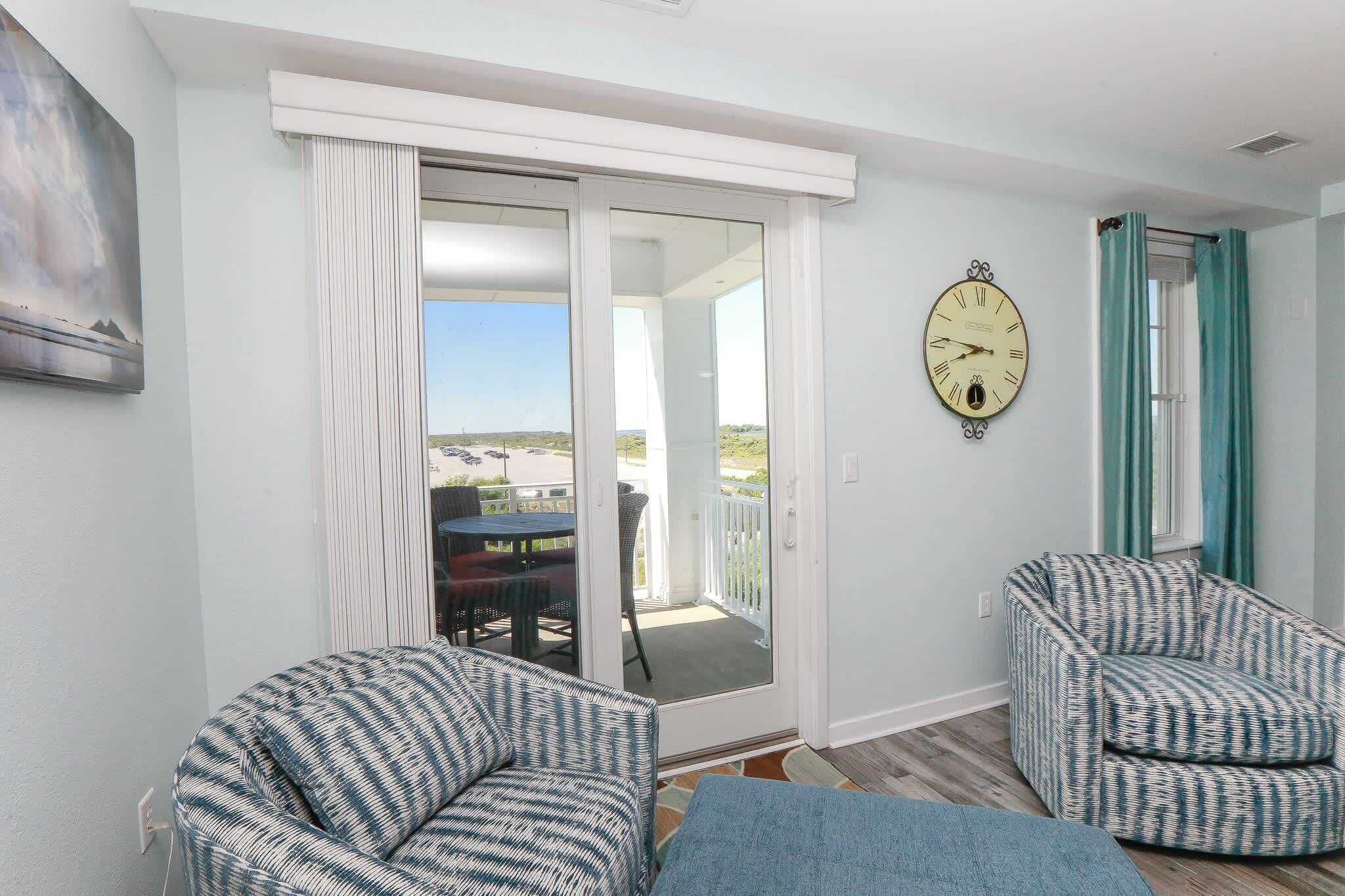 Ein Zimmer mit einer Schiebetür aus Glas zum Balkon, zwei gemusterte Sessel, eine Wanduhr und ein Gemälde.