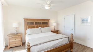 A bedroom with a wooden bed, two bedside tables with lamps, a ceiling fan, and a door.