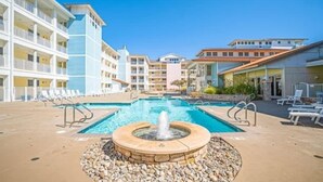 A hotel pool area with a central fountain, multiple balconies, and sun loungers.