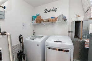 Une buanderie équipée de deux machines à laver, d’une étagère contenant des produits de lessive et d’un panneau fixé au mur sur lequel on peut lire : « Buanderie ».