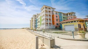 A beachfront hotel with multiple floors, a sandy beach in the foreground, and a clear sky.