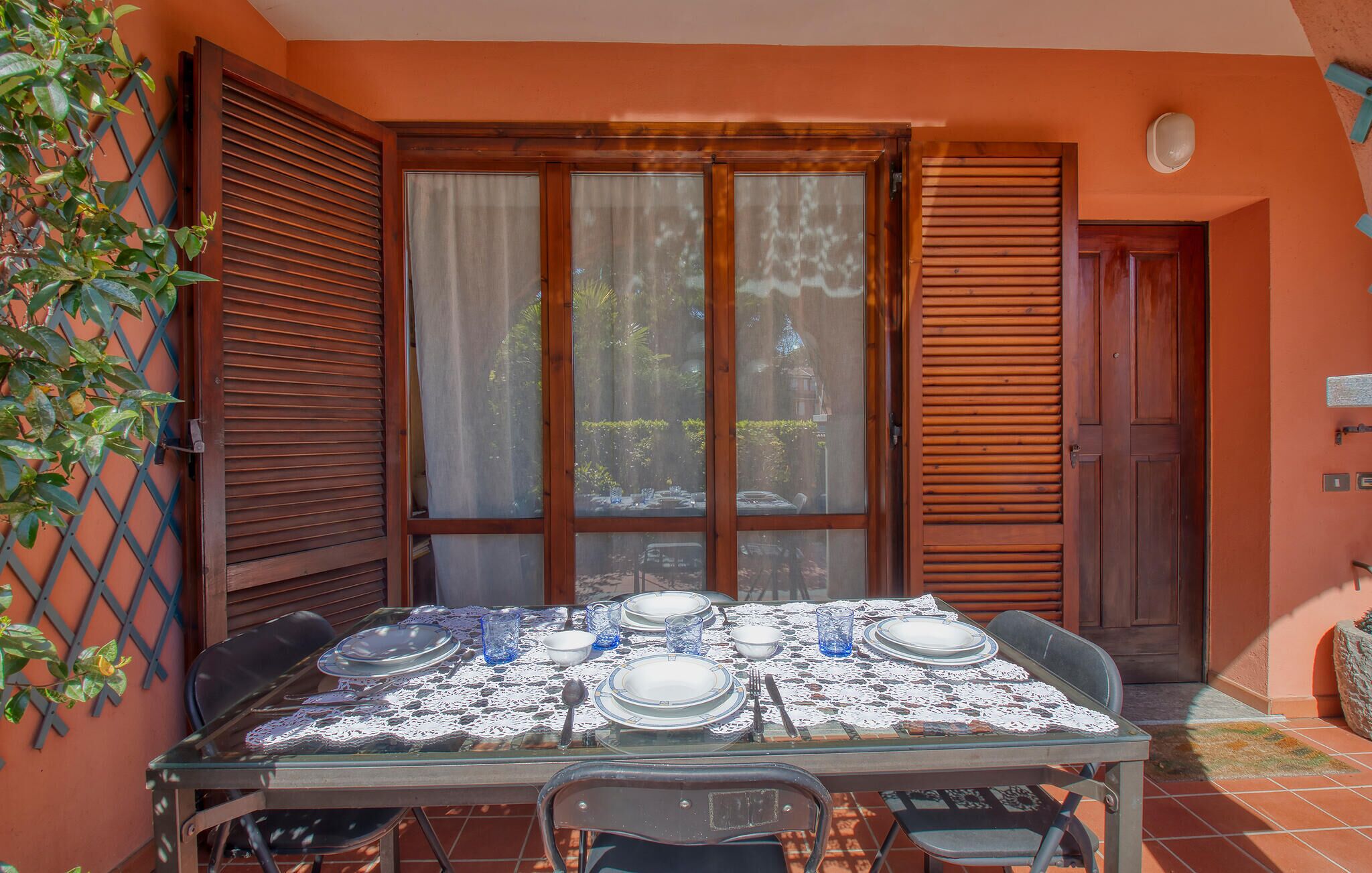 Mesa de jantar posta para quatro pessoas, com toalha de renda, copos e pratos.