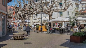 Un área de café al aire libre con mesas y sillas, rodeada de edificios y árboles.