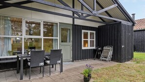 Un edificio con un patio techado que incluye una mesa, sillas, una parrilla y un pequeño jardín.