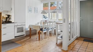 A modern kitchen with white cabinetry, a dining area with a table and chairs, and a view through large windows.