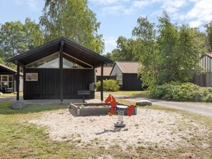 A wooden cabin with a sloped roof, a sandbox with a red toy horse, and a picnic table.