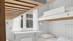 Una habitación compacta con una cama litera, una ventana con cortinas, una lámpara de noche y una estantería empotrada.