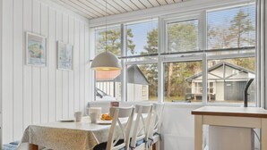 A cozy dining area with a table set for two, a window with a view of a house, and a shelf with kitchen items.