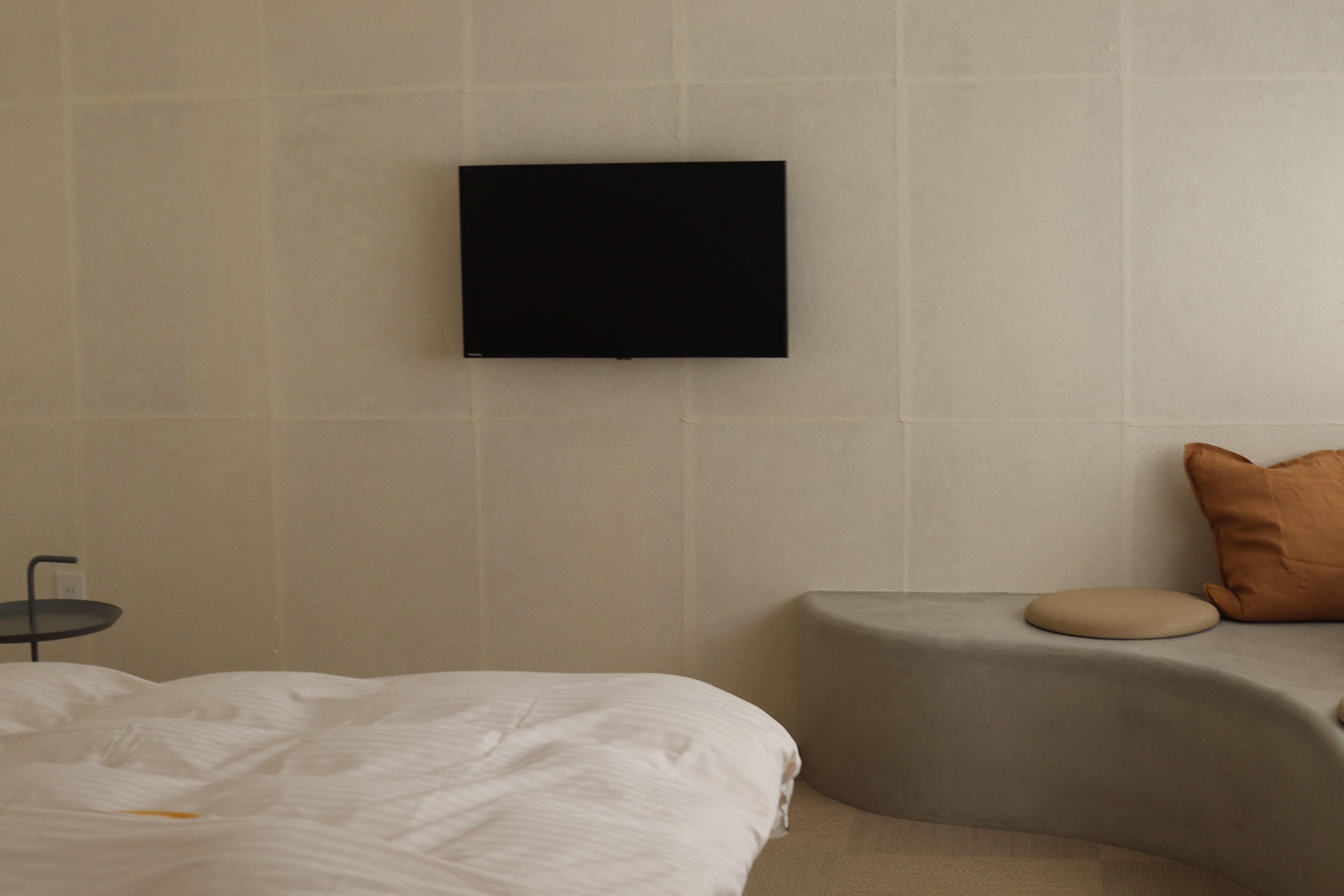 Ein modernes Hotelzimmer mit einem Bett, einem kleinen Nachttisch, einem an der Wand montierten Fernseher und einer gepolsterten Bank.