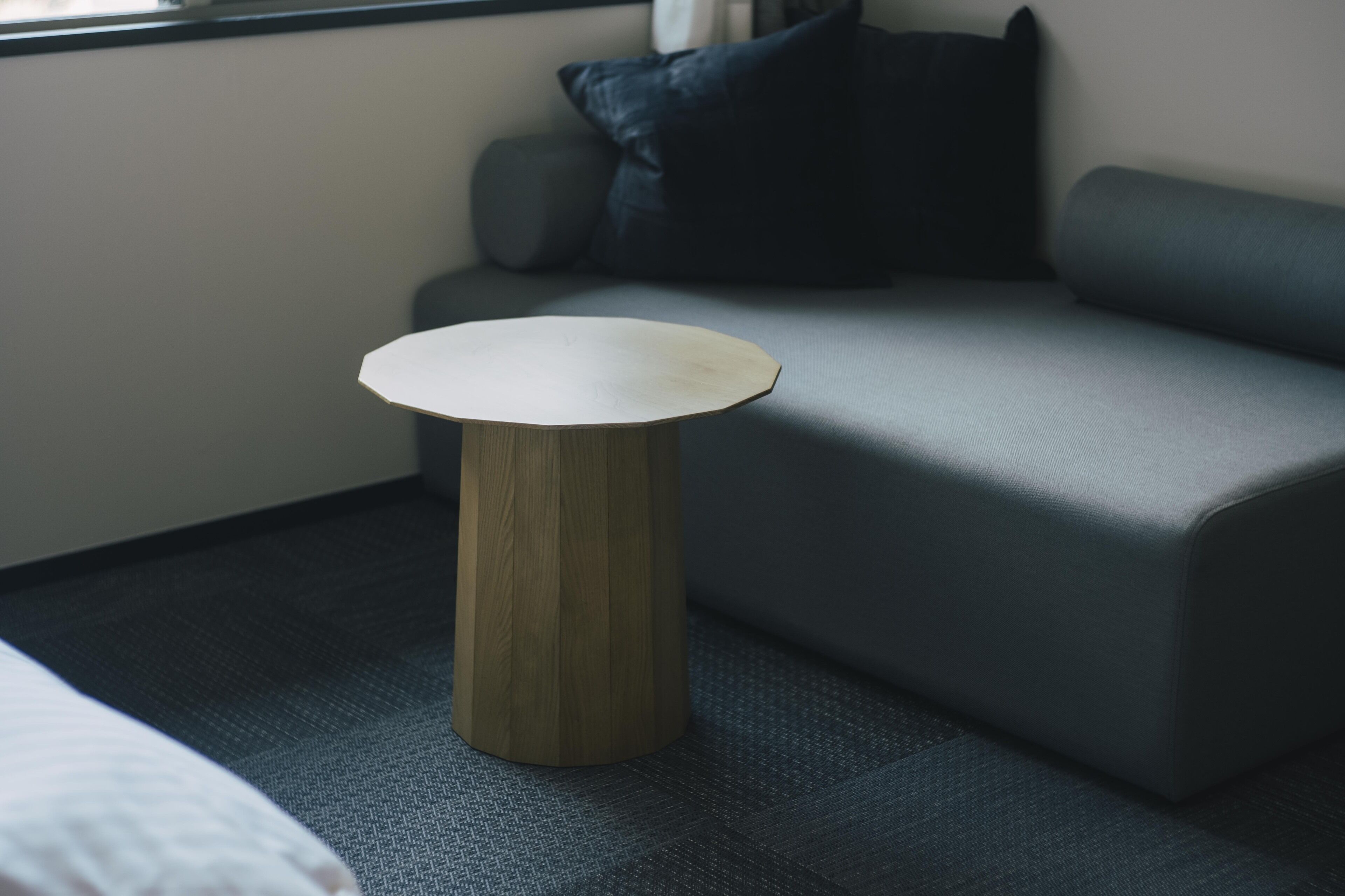 Una habitación moderna con un sofá gris, una mesa redonda de madera y una alfombra gris.