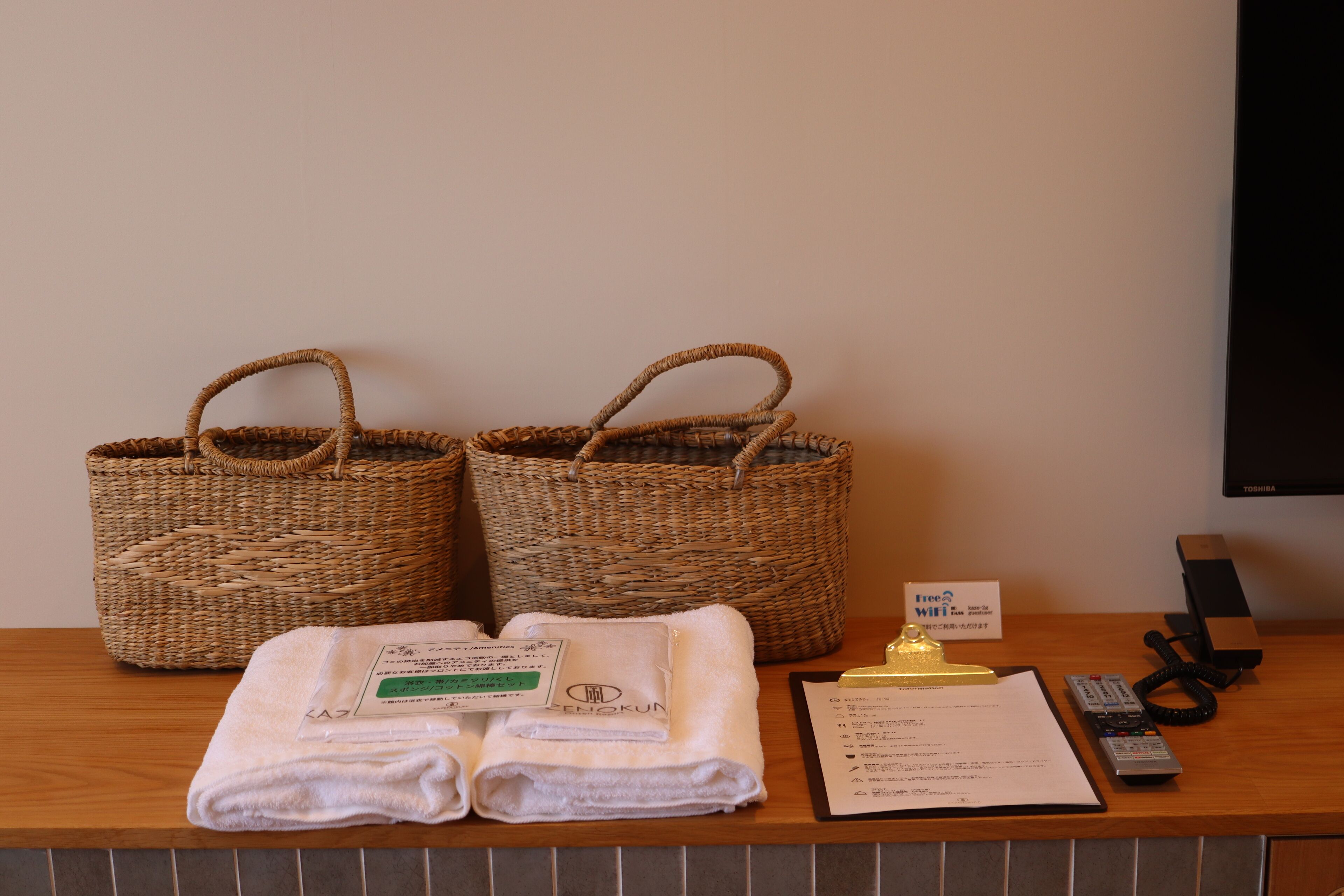 A reception desk with two woven baskets, folded towels, a clipboard with a menu, a sign for free Wi-Fi, a telephone, and a television.