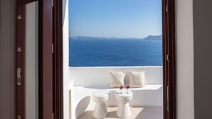 Ein Balkon mit Meerblick, zwei weiße Tische mit Getränken und ein weißes Sofa mit Kissen.
