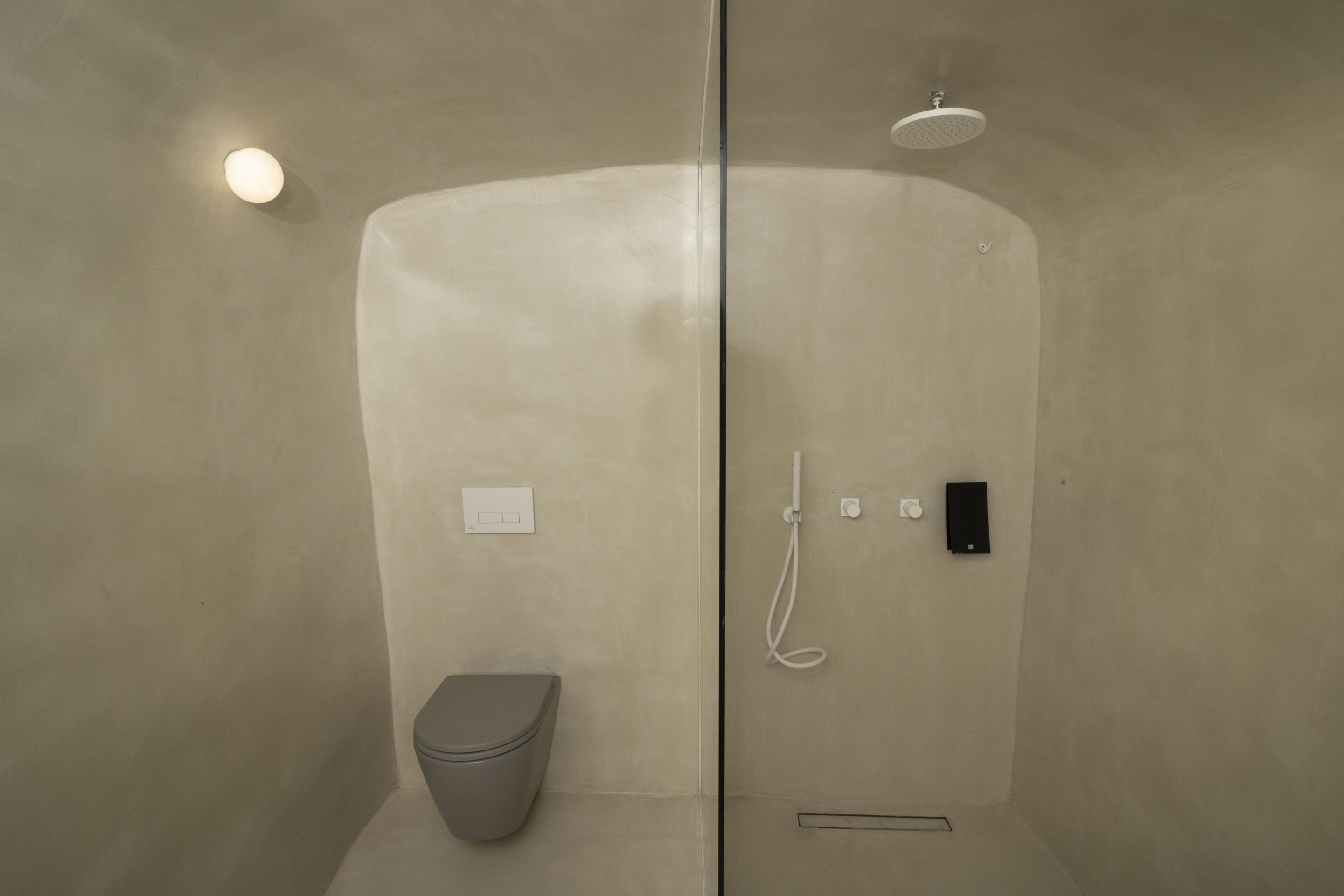Un baño moderno con mampara de vidrio, inodoro, ducha con cabezal de ducha manual y panel de control en la pared.