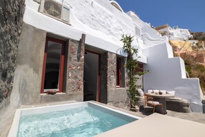 A white-washed building with a stone facade, a swimming pool, and outdoor seating. - Kyrkos Residency (Santorini)