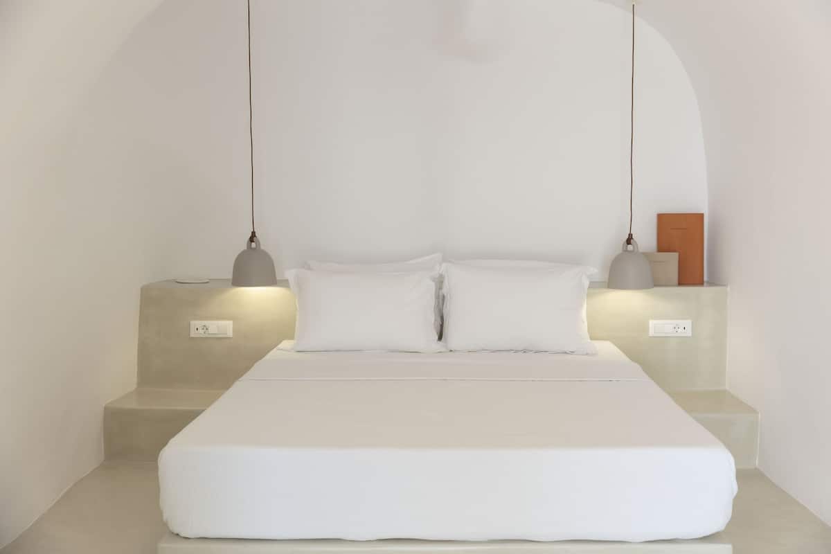 Un dormitorio minimalista con una cama grande, dos mesitas de noche e iluminación colgante.