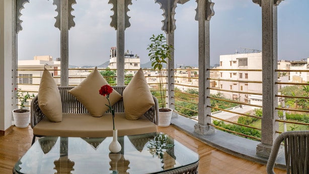 Un balcon avec une table en verre, des sièges confortables et des plantes en pot.