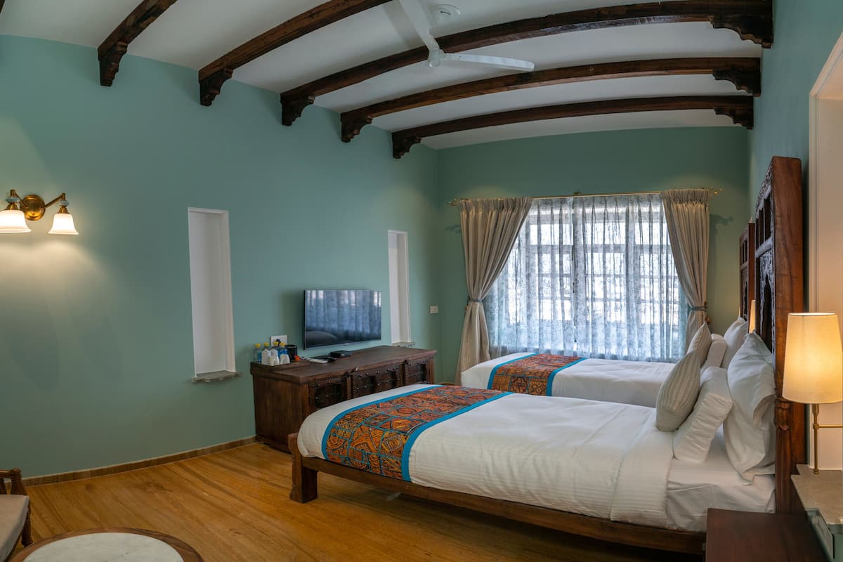 Een kamer met twee bedden, houten balken in het plafond, een televisie en een raam met gordijnen.