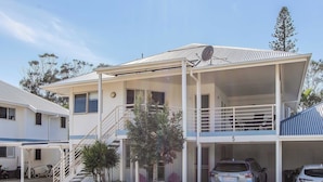 A two-story building with a covered porch, a staircase, and a car parked in the driveway. - Hastings Cove 2 Bedroom Upstairs Estuary Water View Apartment (Tweed)