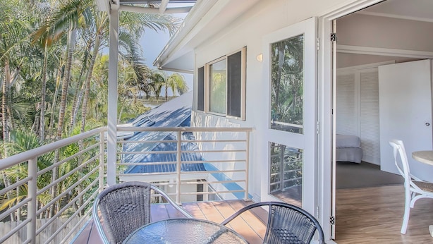 A balcony with a glass table and chairs, overlooking a lush garden with tall palm trees. - Hastings Cove 2 Bedroom Upstairs Estuary Water View Apartment (Tweed)