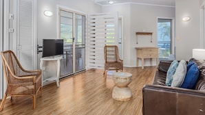 A spacious living area with a wooden floor, a television, wicker chairs, a coffee table, and a sofa with cushions. - Hastings Cove 2 Bedroom Upstairs Estuary Water View Apartment (Tweed)