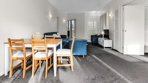 Un soggiorno moderno con zona pranzo, che include un divano, una TV e un armadietto bianco.