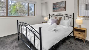 Un letto ben rifatto con lenzuola bianche e cuscini decorativi, una testiera in metallo nero e un comodino con una lampada.