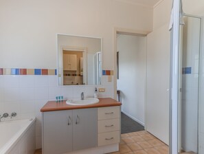 A bathroom with a white sink, a mirror, a bathtub, and a cabinet with drawers.